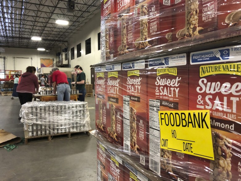 A pallet of food awaits processing as volunteers work in the background to label cans of beans for redistribution at Roadrunner Food Bank in Albuquerque, New Mexico.