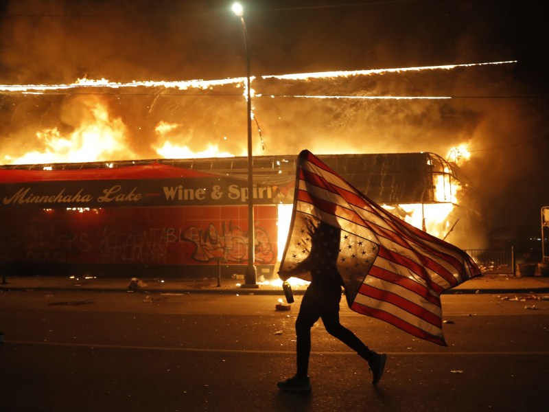 A protester carries a U.S. flag upside down as he walks past a burning building in Minneapolis on May 28, 2020, during a protest over the death of George Floyd.